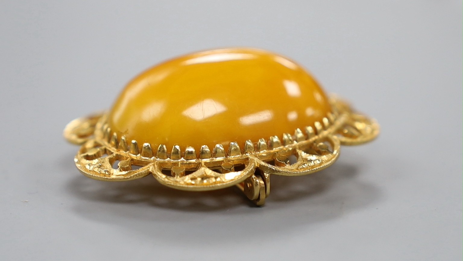 A 22ct mounted oval amber set brooch, 44mm, gross weight 12.1 grams.